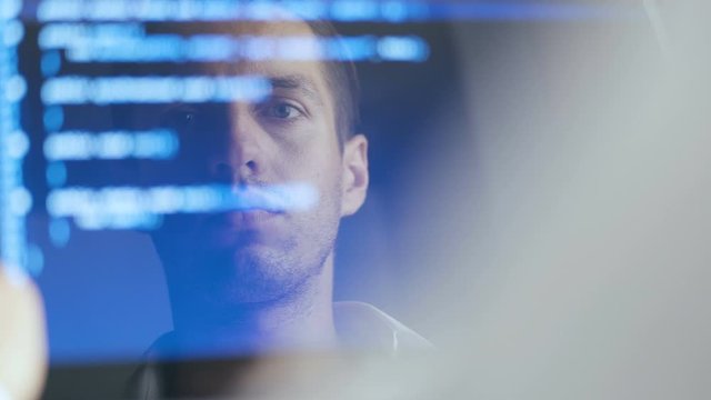 Double Exposure Shot of Man Hacker Programmer working at a laptop. Reflection in monitor: Developer writes blue code.