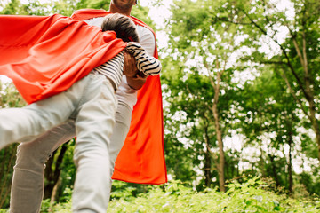 low angle view of father spinning little boy in red superhero cloak