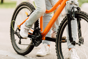 cropped view of son riding bicycle while father standing near kid