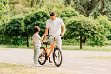 Obraz premium full length view of father checking bicycle while son standing near dad