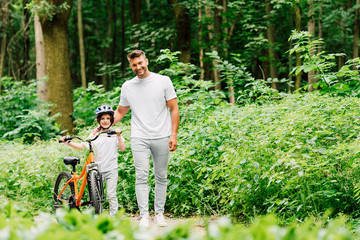 full length view of father and son standing and looking at camera while boy holding bicycle
