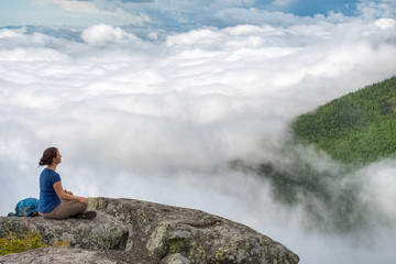Lone meditating woman at the edge of the cliff, above the clouds