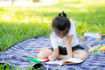 Young little asian girl reading and writing book in the park, asia kid homework and study in the...