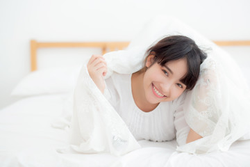 Obraz na płótnie Canvas Beautiful portrait young asian woman lying and smile while wake up with sunrise at morning, girl with happy annd fun in the bedroom, lifestyle and relax concept.