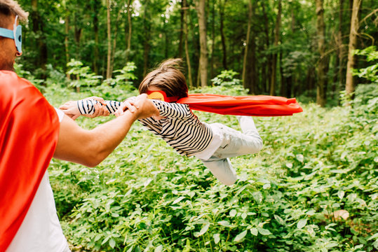 father in superhero costume spinning around son in red cloack