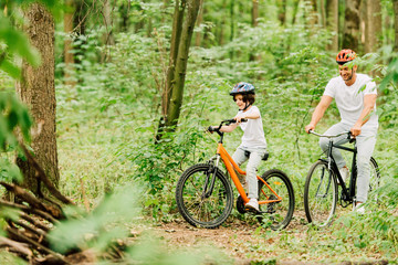 Fototapeta premium Selective focus of father and son in helmets riding bicycles around forest