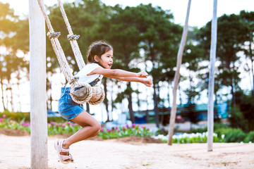 Fototapeta na wymiar Happy asian child girl having fun to play on wooden swings in playground with beautiful nature
