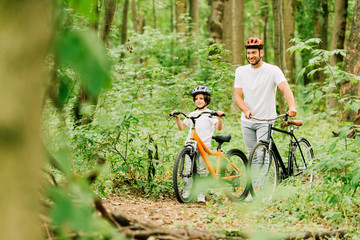 selective focus of father and son walking with bicycles in forest