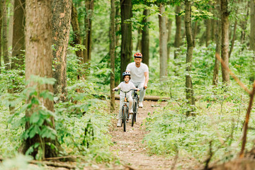 Obraz premium full length view of father and son riding on path in forest