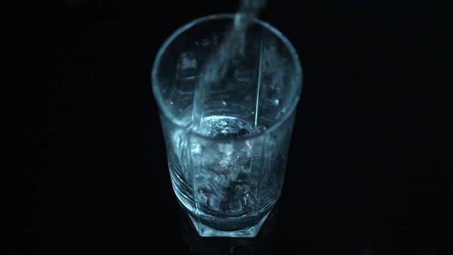 Clean water pouring in empty glass, black backdrop, locked off