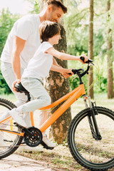 side view of son riding bicycle and father walking next to kid and holding sit of bike