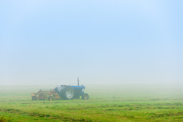 Fototapeta na wymiar Blue tractor sitting in an empty foggy field in the morning.