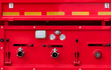 Fire truck. Rescue engine. Side view of red firetruck vehicle. Fire department truck. High pressure fire safety pump, gauge pressure, and valve lever on firetruck. Reflective tape for safety on truck.