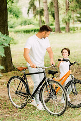 Obraz premium full length view of father and son with bicycles looking at each other
