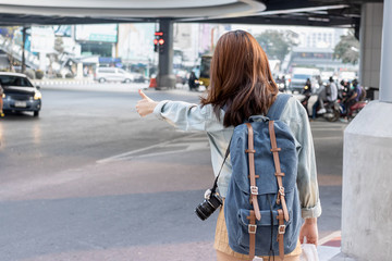 Back view of young Asian travel girl hitchhiking on the road in city. Life is a journey concept.