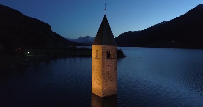 Ascending Aerial: The Picturesque Lake Reschen Bell Tower at Night With Hills and Mountains - South Tyrol, Italy