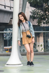 Portrait of young Asian woman tourist leaning against a pole outdoors in urban. Travel and vacation concept.
