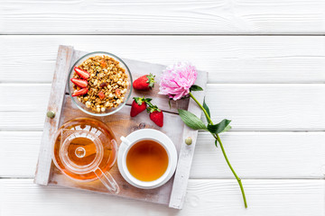 granola, tea and fruit for homemade breakfast on the tray on white wooden background top view