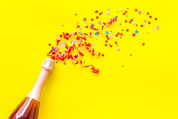 Champagne bottle with colorful party streamers for celebration on yellow background top view mockup