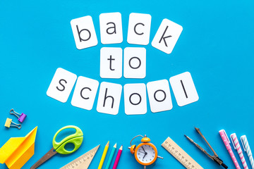 Back to school with stationary, scissors and alarm clock on blue student desk background top view