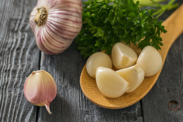 Peeled cloves of garlic in a wooden spoon and a whole garlic on a black wooden table. Component of traditional medicine.