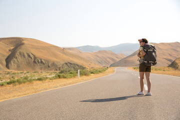 Hitchhiker traveler woman on the road in sunset. Girl traveler hiker on the road. Summer vacation. Freedom.