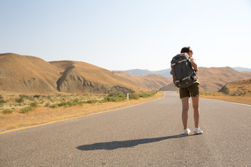 Obraz premium Hitchhiker traveler woman on the road in sunset. Girl traveler hiker on the road. Summer vacation. Freedom.