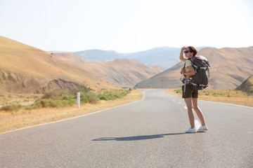 Hitchhiker traveler woman on the road in sunset. Girl traveler hiker on the road. Summer vacation. Freedom.