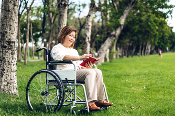 Senior adult elderly asia women sit on wheelchair and reading book outdoor