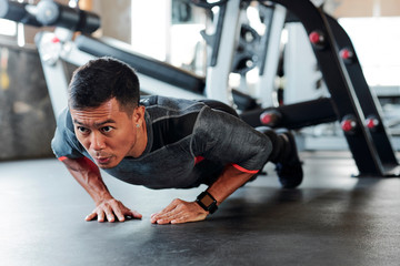 Strong fit young Asian man doing diamond push-ups in gym during sports training - obrazy, fototapety, plakaty