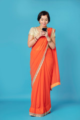 Smiling lovely young Indian woman in beautiful sari dress checking messages on her smartphone