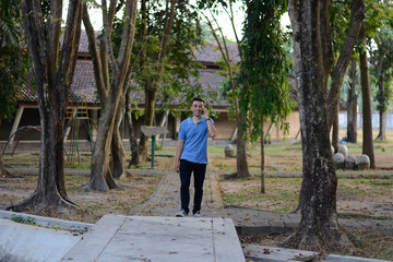 Portrait of handsome Asian male in blue t-shirt talk at phone in outdoor parks