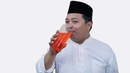 Fototapeta premium portrait of overweight muslim man with head cap or songkok drink a large glass of tea to break the fast