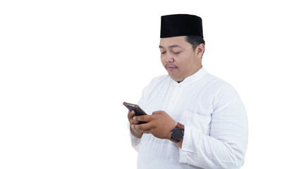 chubby overweight muslim asian man with baju koko and peci use smart phone and smile at camera