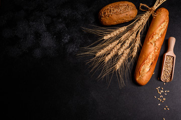 Fresh fragrant bread with grains and cones of wheat against a dark background. Assortment of baked...