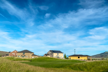 Grassy terrain and houses under blue sky with white clouds on a sunny day