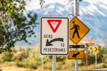 Yield Here To Pedestrians sign against trees and mountain viewed on a sunny day