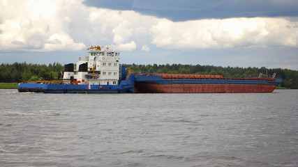 White blue tugboat pushes a blue red empty barge along the river on the background of sky with cloud and  forest Bank - commercial shipping, Maritime logistics