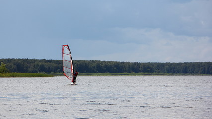 Windsurfing on a Board with a transparent sail riding on the lake against the green shore - outdoor activities, extreme water sports, beautiful river landscape