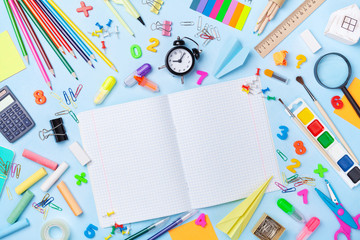 School supplies and stationery with open notebook on blue table top view. Education, learning and back to school concept.