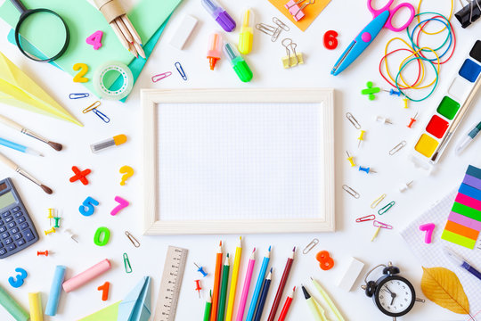 Empty wooden frame with squared paper, alarm clock, different stationery and colorful supplies on white background. Back to school concept. Top view.