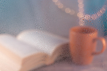 ventana mojada y taza de café con un libro