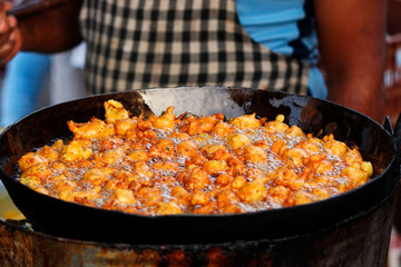 Man frying spicy snack or entree dish similar to a fritter, bhajji on street