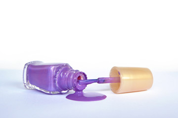 Open purple nail polish bottle lying on side with spilled nail polish pouring out on white background