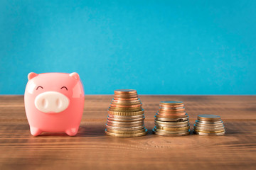 Little piggy Bank and a few stack coins on the wooden table. Close up. The concept of saving money.
