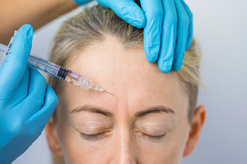 Doctor makes the rejuvenating facial injections for smoothing woman's forehead skin - obrazy, fototapety, plakaty
