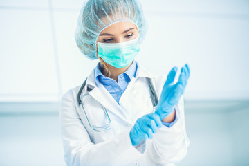 Doctor woman surgeon specialist in sterile clothing putting on surgical gloves - obrazy, fototapety, plakaty