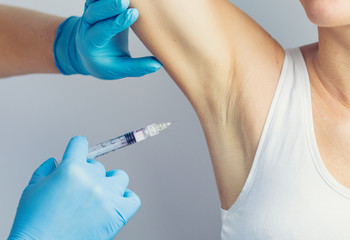 The doctor making intramuscular injection with syringe of botulinum toxin in the armpit against hyperhidrosis.