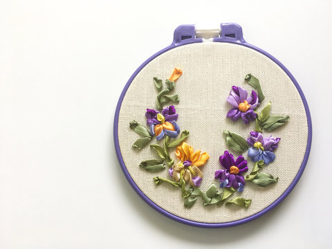 Handmade embroidery with satin ribbons of floral ornament from yellow and violet pansies on a white background. Flat lay, copy space, close up, plase for text (the embroidery made the author of photo)
