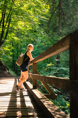 Hiking in an idyllic forest: Young girl is standing on a wooden footbridge and enjoys the view